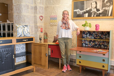 L'artisane de l'Atelier de Cilou pose au milieu de meubles vintage relookés aux tiroirs multicolores