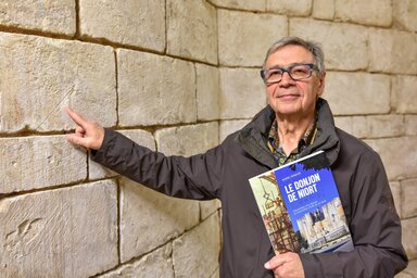 Daniel Courant, son livre à la main, montre une marque gravée dans la pierre