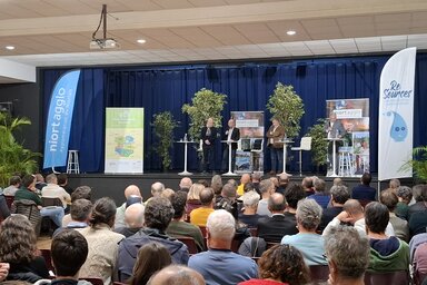 Quatre intervenants sur scène devant un large public réuni en salle pour une conférence de Niort Agglo