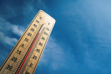 Thermomètre en bois affichant plus de 33 °C sur fond de ciel bleu, évoquant une vague de chaleur