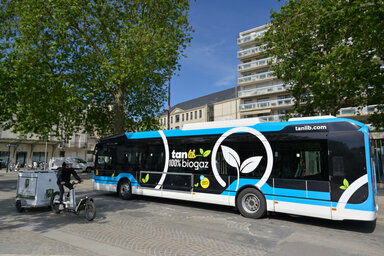 Bus articulé roulant au biogaz portant le marquage « TanLib 100 % biogaz », stationné sur la place de la Brèche