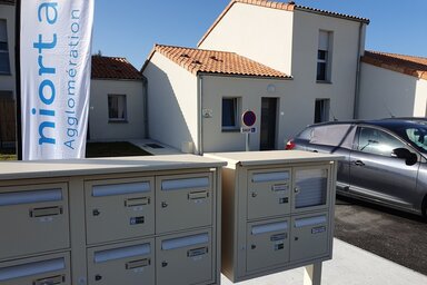 Boîtes aux lettres collectives devant des maisons individuelles neuves, avec la bannière Niort Agglomération