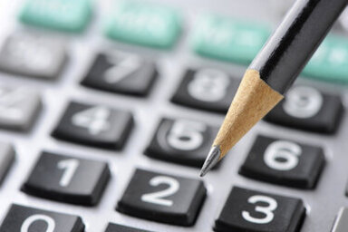 Crayon à mine posé sur le clavier d'une calculatrice en gros plan, évoquant un travail de calcul financier